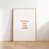 “Focus on the Lord” Christian text art, printable PDF/JPG, lightwood frame on wood floor.