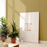 “Focus on the Lord” Christian artwork in sunlit room with plants.